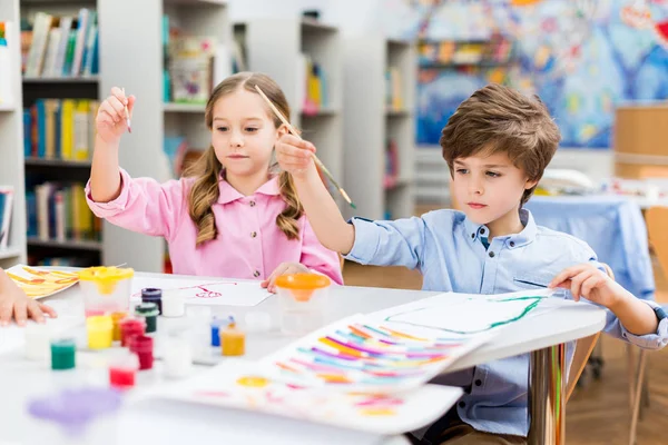 Simpatici bambini che tengono pennelli colorati barattoli di guazzo e carte — Foto stock