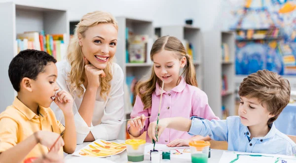 Plan panoramique de femme heureuse regardant la caméra près des enfants mignons — Photo de stock