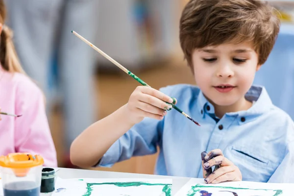 Messa a fuoco selettiva del bambino felice che tiene pennello vicino a carta e bambino — Foto stock
