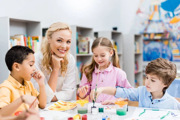 Selektiver Fokus einer glücklichen Frau, die in die Kamera schaut, in der Nähe niedlicher Kinder — Stockfoto