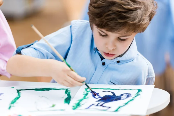 Selective focus of cute kid holding paintbrush and looking at paper — Stock Photo