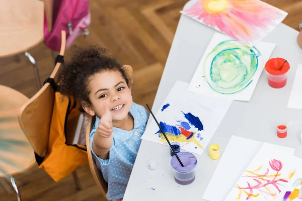 Vue aérienne d'heureux gamin afro-américain pointant du doigt près du papier avec peinture — Photo de stock