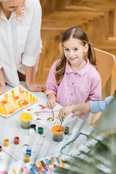 Vista aérea del niño feliz sonriendo mientras mira a la cámara cerca del maestro - foto de stock