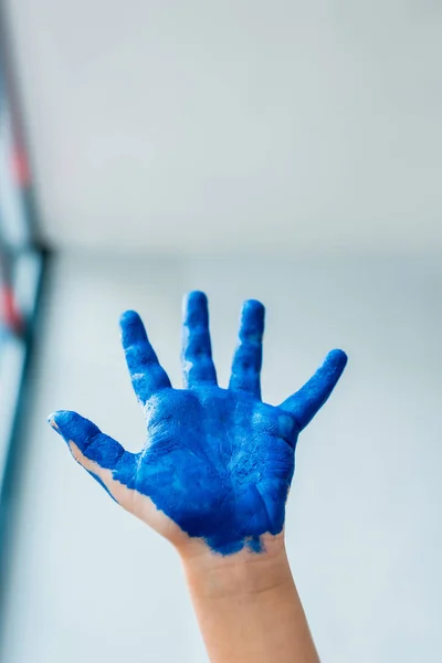 Cropped view of kid showing painted hand with blue gouache paint — Stock Photo