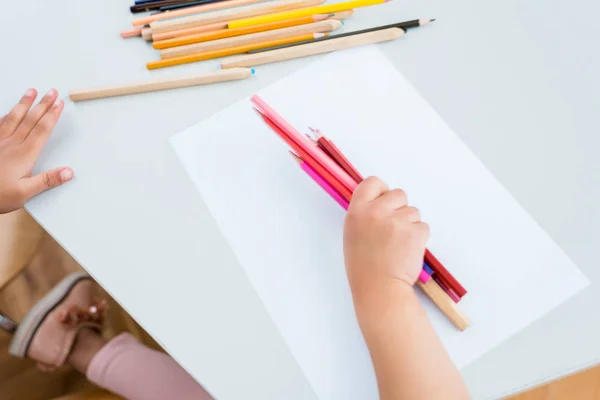 Обрізаний вид дитини, що тримає барвисті олівці біля паперу — стокове фото