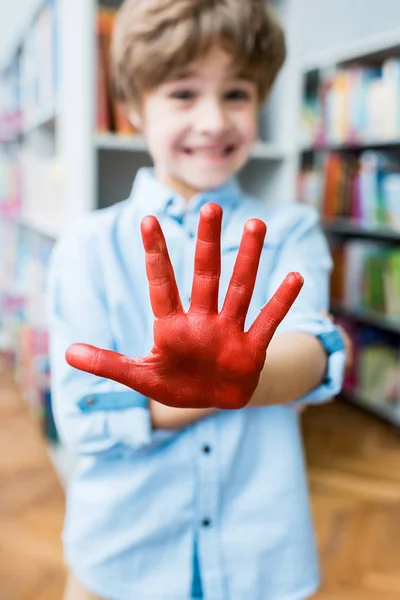 Enfoque selectivo de niño feliz mostrando la mano pintada con pintura gouache rojo - foto de stock