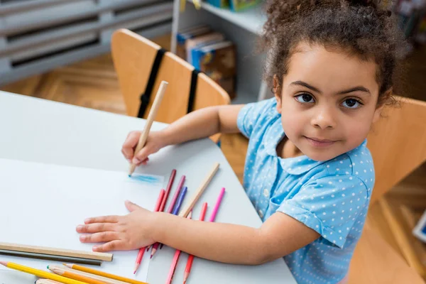 Vista aérea de adorable niño afroamericano dibujo en papel en blanco - foto de stock