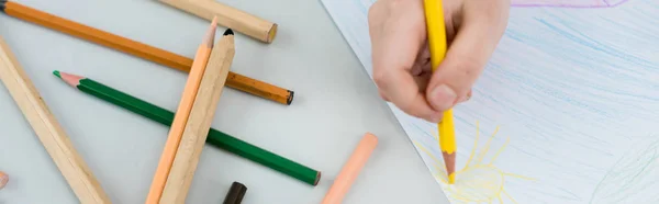 Panoramic shot of kid drawing with yellow pencil on paper — Stock Photo