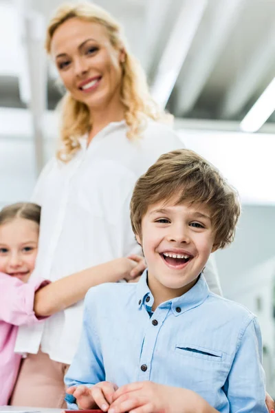 Selektiver Fokus eines fröhlichen Kindes, das lächelt, während es in die Kamera in die Nähe einer Frau blickt — Stockfoto