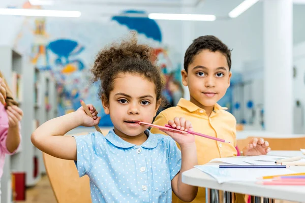 Selektiver Fokus des süßen afrikanisch-amerikanischen Kindes, das den Bleistift in der Nähe des entzückenden Kindes beißt — Stockfoto