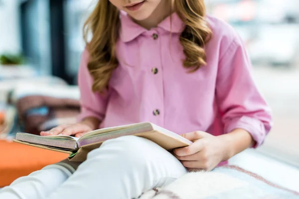 Cropped view of child sitting and reading book in library — Stock Photo