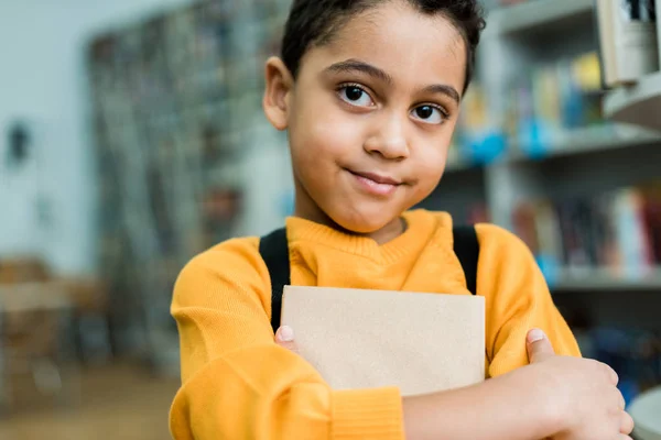 Entzückendes afrikanisches amerikanisches Kind hält Buch in der Hand und blickt in die Kamera — Stockfoto