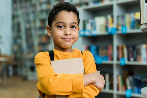 Lindo africano americano niño sosteniendo libro y mirando a la cámara - foto de stock