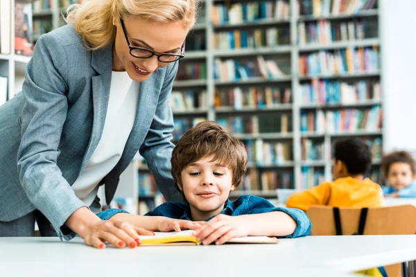 Schöne Frau, die neben niedlichem Kind steht, das Buch liest — Stockfoto