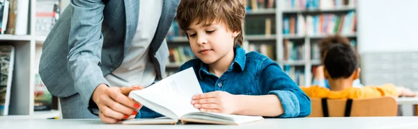 Plano panorámico de la mujer de pie cerca lindo niño leyendo libro - foto de stock