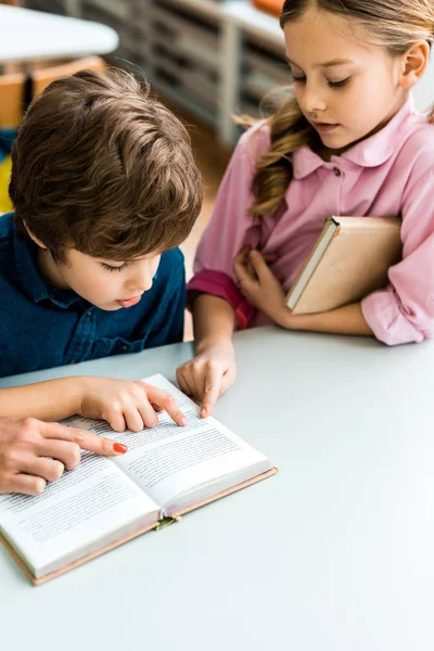 Vista recortada de la mujer señalando con el dedo en el libro cerca de los niños lindos - foto de stock