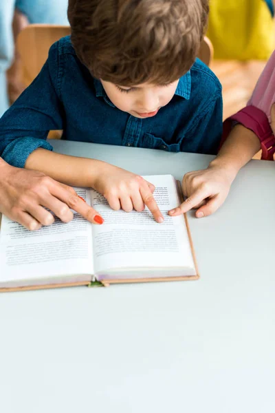 Recortado vista de la mujer y el niño señalando con los dedos en el libro cerca de chico lindo — Stock Photo