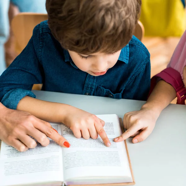 Обрезанный вид женщины и ребенка указывая пальцами на книгу рядом с мальчиком — стоковое фото