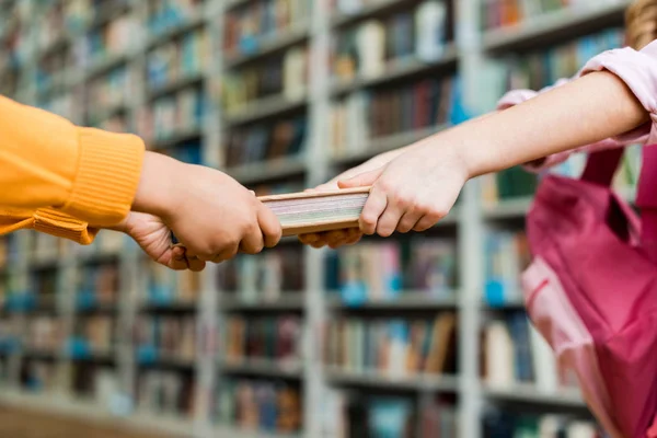 Vista cortada de crianças puxando livro enquanto em pé na biblioteca — Fotografia de Stock