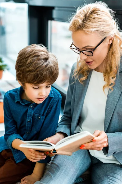 Selective focus of woman in glasses reading book with cute kid — Stock Photo