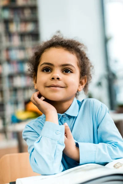 Enfoque selectivo de niño americano africano alegre sonriendo cerca de libro en la mesa - foto de stock