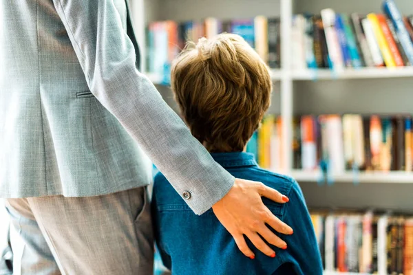 Вид сзади ребенка, стоящего с женщиной в библиотеке — стоковое фото
