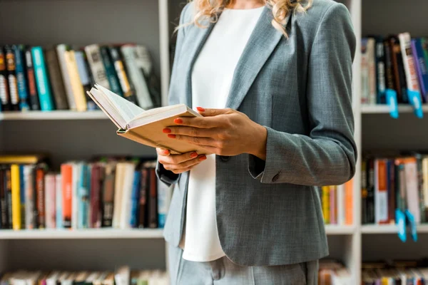 Vista ritagliata di donna che tiene libro e in piedi in biblioteca — Foto stock