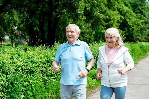 Cheerful senior man running near wife in park — Stock Photo