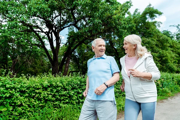Веселий старший чоловік дивиться на дружину під час бігу в парку — стокове фото