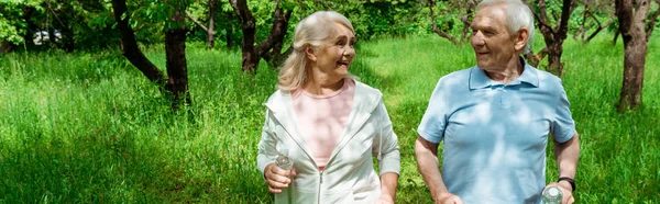 Plan panoramique de femme gaie avec les cheveux gris regardant mari tout en courant dans le parc — Photo de stock