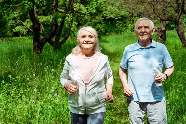 Cheerful woman and man with grey hair running in park — Stock Photo