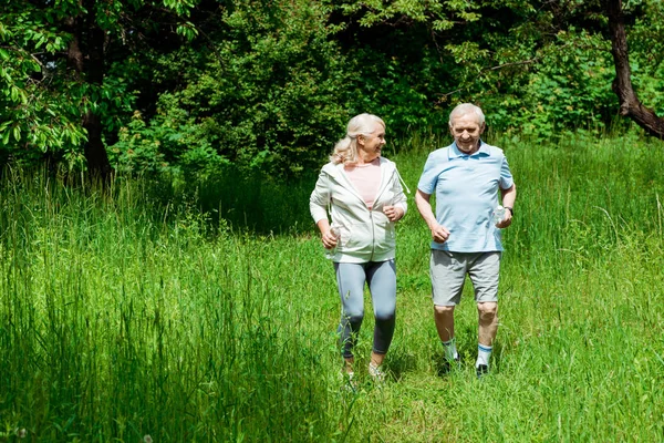 Donna anziana con i capelli grigi guardando il marito mentre corre nel parco — Foto stock