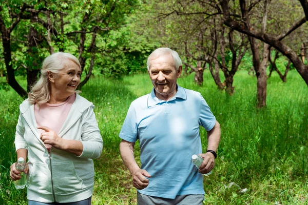 Старшая счастливая женщина смотрит на мужа с седыми волосами во время бега в зеленом парке — стоковое фото