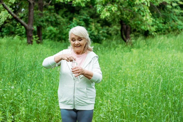 Fröhliche Seniorin öffnet Flasche mit Wasser im Park — Stockfoto