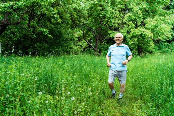 Счастливый пожилой человек с седыми волосами бегает по зеленому парку — стоковое фото