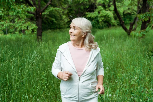 Happy senior woman with grey hair running in green park — Stock Photo