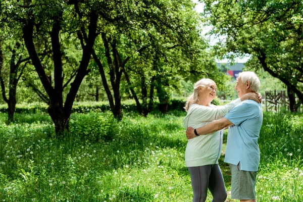 Cheerful retired man hugging senior wife in green park — Stock Photo