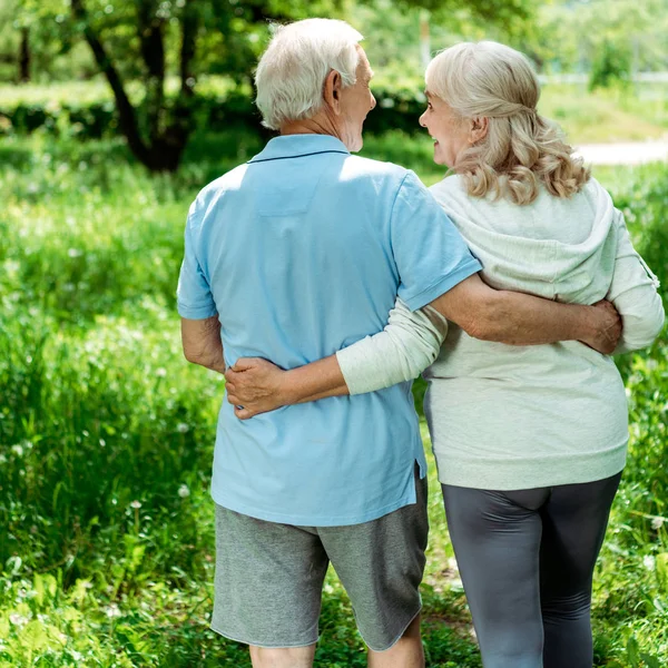 Alegre retirado hombre abrazando feliz senior esposa en verde parque - foto de stock