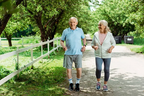 Cheerful retired woman running near senior husband in park — Stock Photo