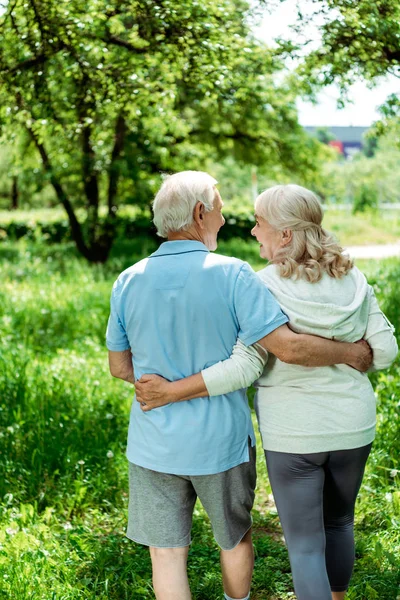 Cheerful pensioner hugging happy senior wife in green park — Stock Photo