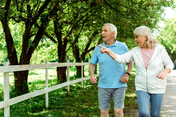 Retired woman with grey hair pointing with finger near surprised husband — Stock Photo