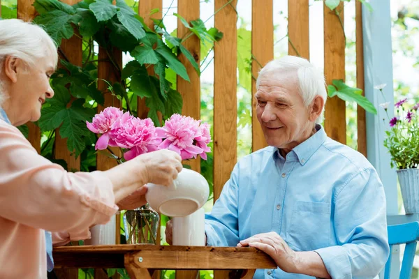 Niedrigwinkel-Ansicht der fröhlichen Seniorin hält Teekanne in der Nähe Tasse und glücklichen Ehemann — Stockfoto