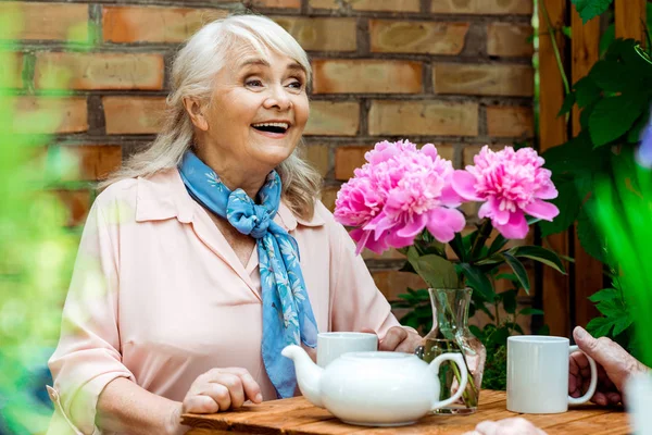 Selektiver Fokus einer glücklichen Rentnerin, die neben rosa Blumen lächelt — Stockfoto