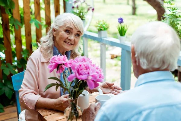 Вибірковий фокус щасливої старшої жінки, дивлячись на чоловіка біля рожевих квітів — стокове фото