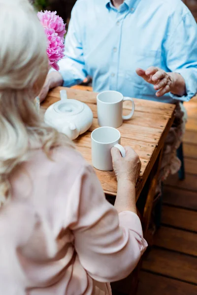Cropped view of senior couple sitting near teapot and cups — Stock Photo