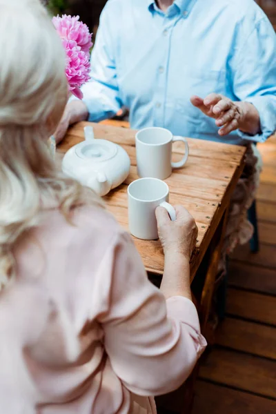 Vue recadrée du couple âgé assis près de la théière et des tasses — Photo de stock