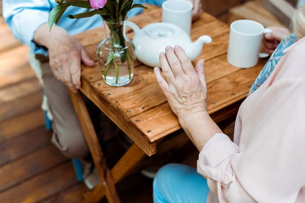 Vue recadrée du couple retraité assis près de la théière et des tasses — Photo de stock