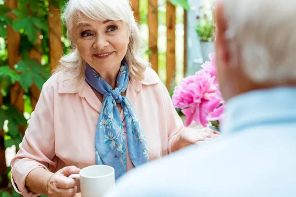 Selektiver Fokus einer glücklichen Seniorin, die ihren Mann ansieht, während sie eine Tasse hält — Stockfoto