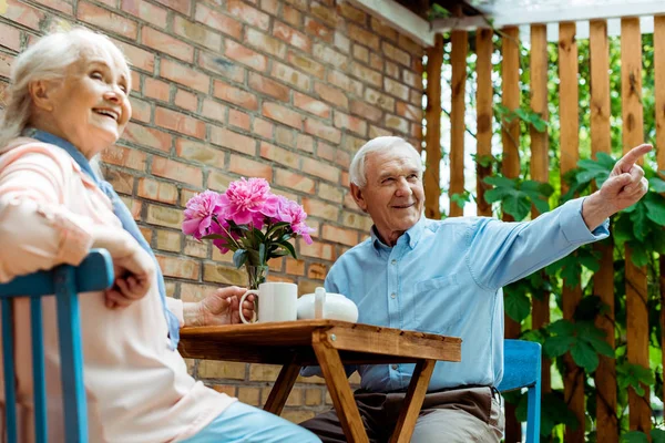 Tiefansicht eines glücklichen älteren Mannes, der mit dem Finger auf seine fröhliche Frau zeigt — Stockfoto