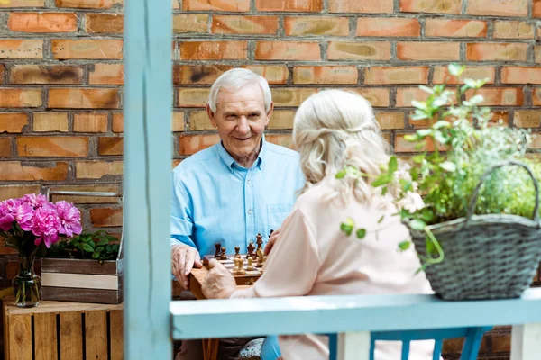 Избирательный фокус счастливого пожилого мужчины, играющего в шахматы с женой — стоковое фото